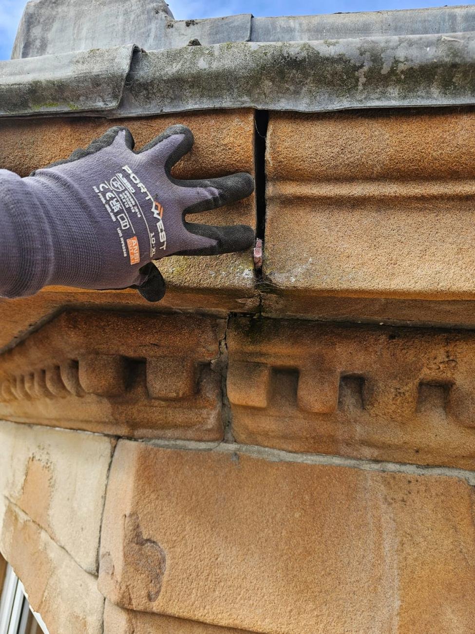 Gloved hand checking a crack in a carved sandstone cornice