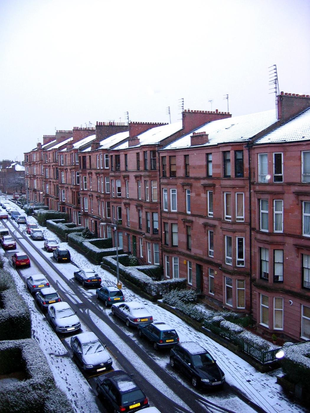 Snow on the roofs of a long street of red sandstone tenements